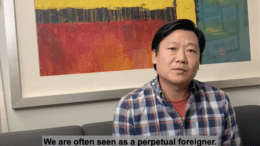 An East Asian man sits in front of a painting